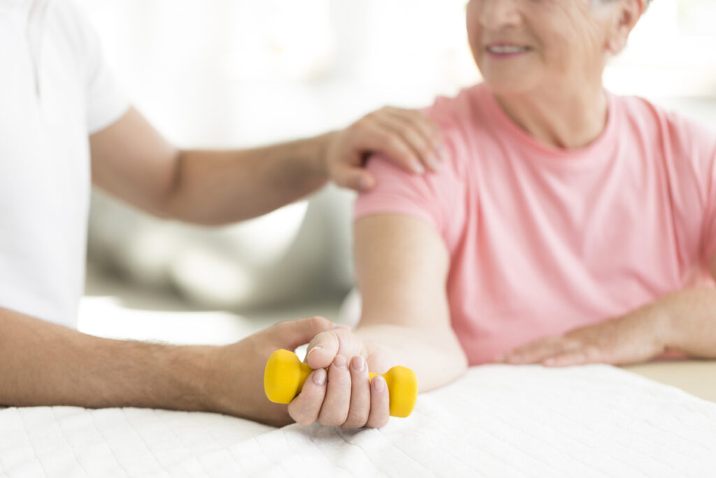 Eine ältere Patientin absolviert gemeinsam mit ihrem Rehabilitationsarzt im Pflegeheim eine aktive isometrische Trainingseinheit